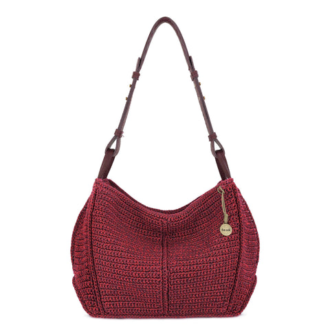 Hand-crochet burgundy hobo bag with blue peace sign medallion and tassel, worn on shoulder.